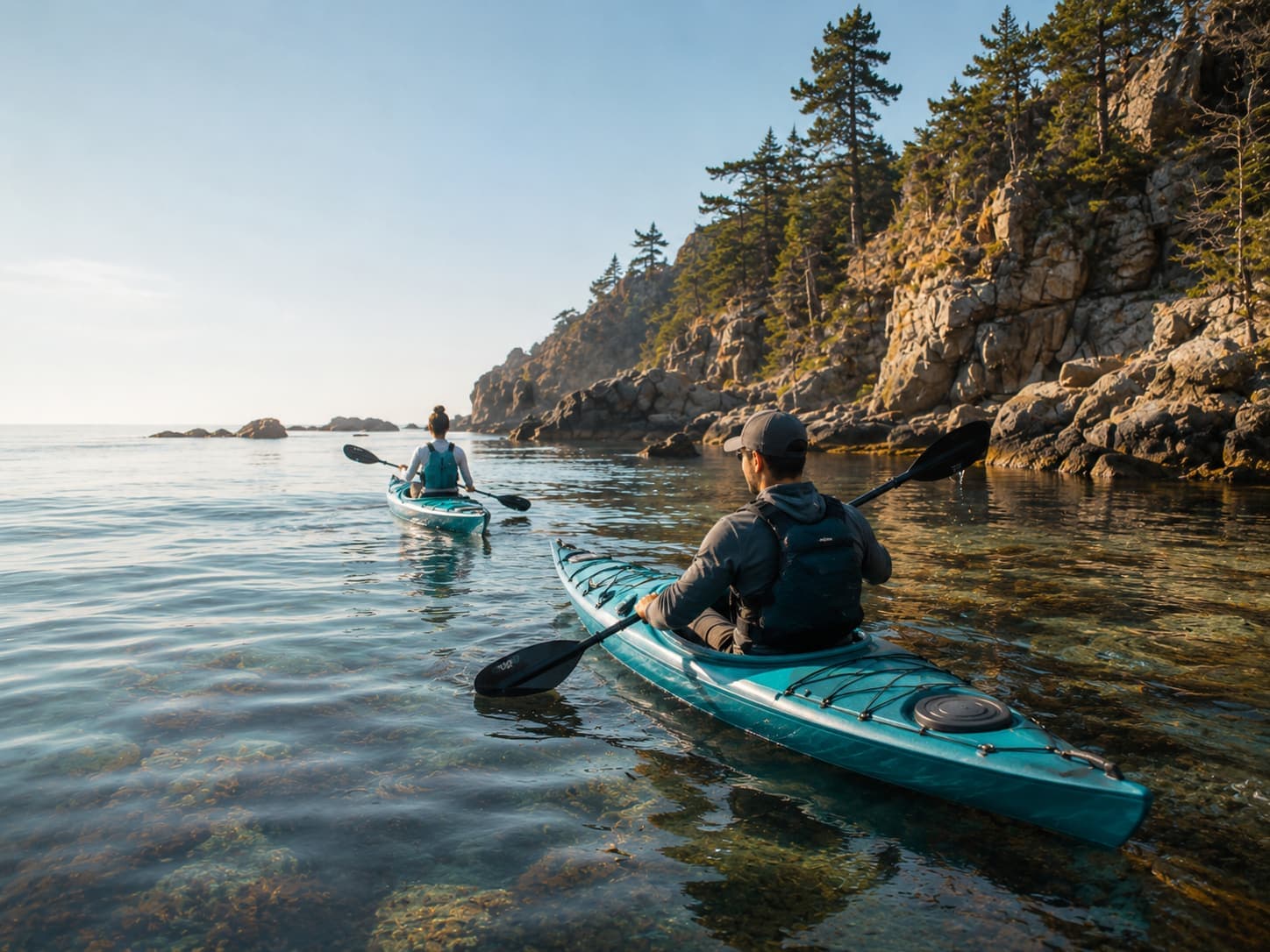 Two kayakers paddling along a rocky coastline in clear water