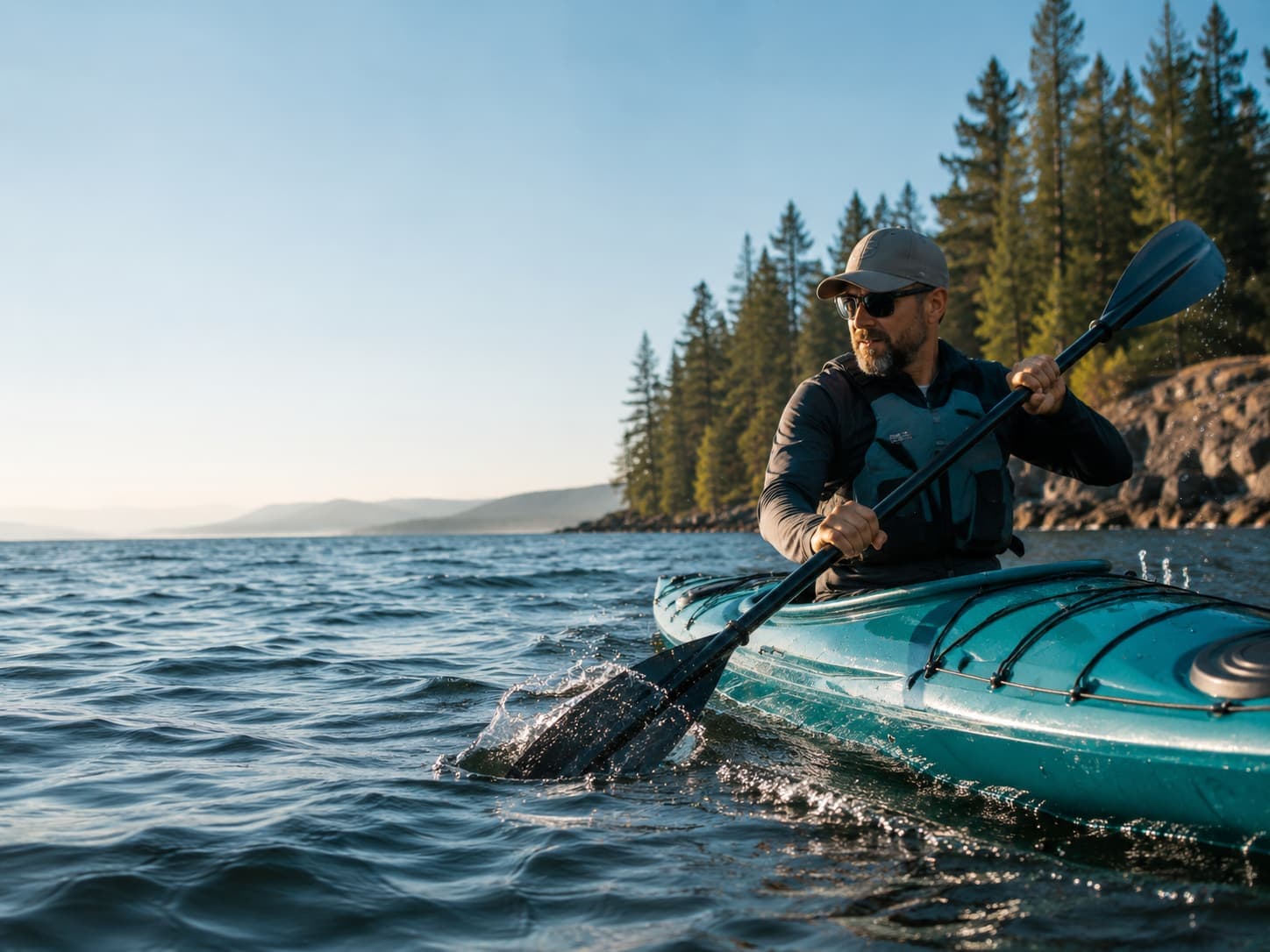 Kayaker paddling a teal kayak across open water with a paddle splash